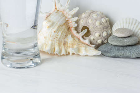 long glass of water on white wooden desktop with spa stones , seashellの写真素材