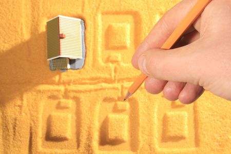 Little house on yellow sand. Hand holding pencil.の写真素材