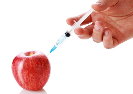 Closeup of a delicious, ripe red apple being injected by a medical syringe or hypodermic needle.の写真素材