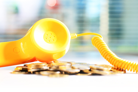 Yellow phone and coins on white tableの写真素材