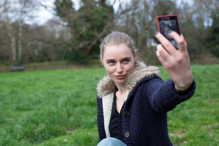 Attractive young woman taking a selfie on her mobile phone as she enjoys a relaxing day walking in the countrysideの写真素材