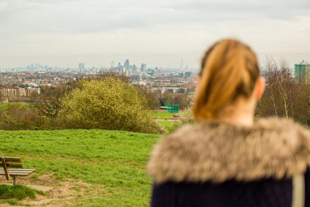Woman standing with her back to the camera looking out over lush green countryside towards a distant townの写真素材