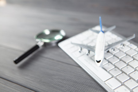 plane, magnifier and keyboard. online search for airline tickets on gray wooden tableの写真素材