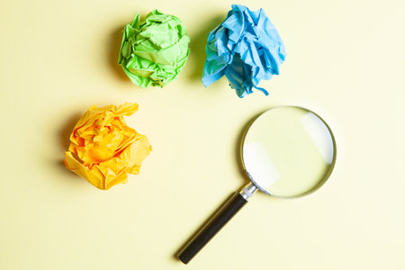 magnifying glass and lumps of papers on yellow backgroundの写真素材
