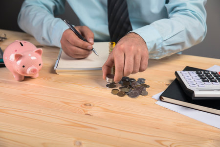 makes calculations and writes in a notebook and next to a piggy bank and coins