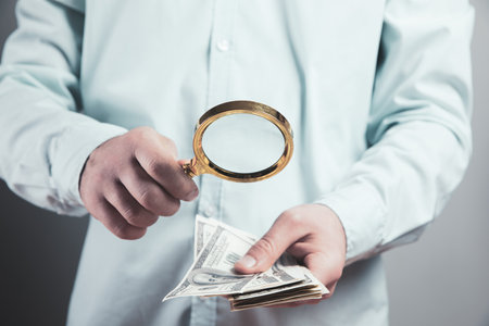 young man checks money with a magnifying glassの写真素材