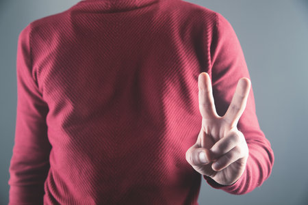 young guy shows peace sign on gray backgroundの写真素材