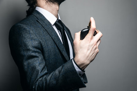 man in a suit and glasses sprinkles with perfume on a gray backgroundの写真素材