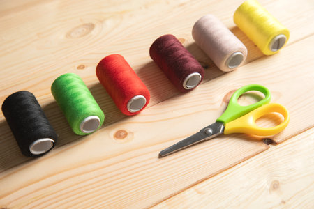 multicolored threads and scissors on wooden background