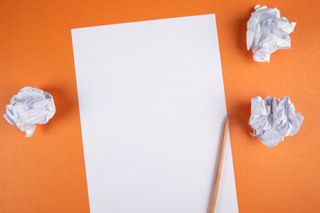 paper with pencil and wad of papers on orange backgroundの写真素材