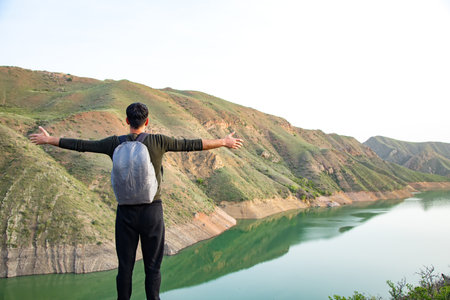 a man stands with open hands on a cliff by the lakeの写真素材