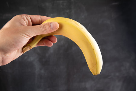 holding a yellow banana on a dark backgroundの写真素材