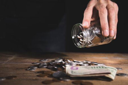 a man spills coins from a glass jar on a wooden tableの写真素材