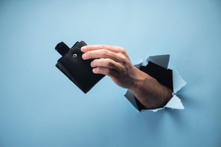Man's hand holding wallet on blue background