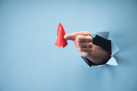 Human hand holding red aids bow on blue backgroundの写真素材