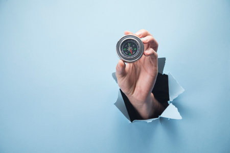 Man's hand holding a compass on a blue backgroundの写真素材