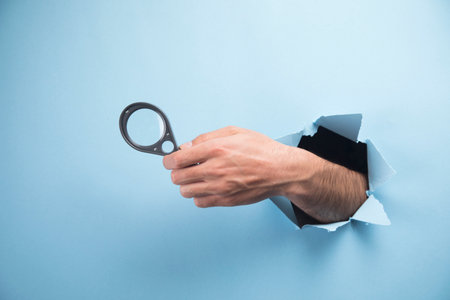 Man's hand holding a magnifying glass on a blue backgroundの写真素材