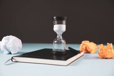 pen, notebook, wad of papers and hourglass on the tableの写真素材