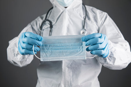 a doctor in a white protective uniform holds a mask on a gray backgroundの写真素材