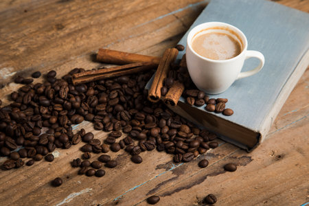 a cup of coffee, coffee seeds, cinnamon and a book on a wooden tableの写真素材