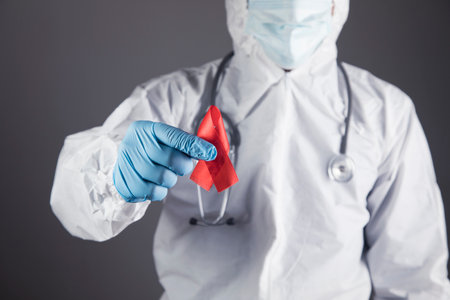 a doctor in a white protective uniform holds a red ribbon on a gray backgroundの写真素材