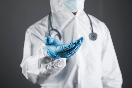 doctor in protective uniform shows open palms. hands in the form of a stand on a gray backgroundの写真素材