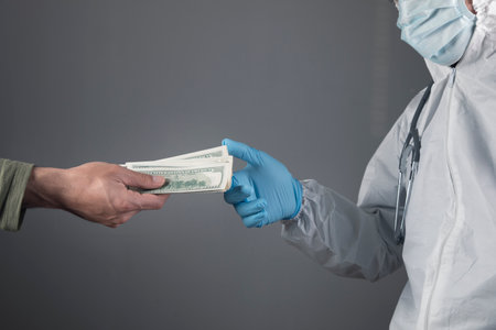 a man gives money to a doctor on a gray backgroundの写真素材
