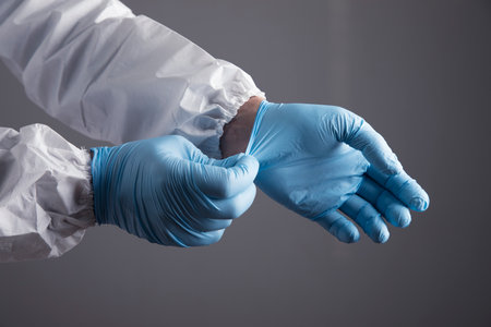 a doctor in a white protective uniform puts on a glove on a gray background