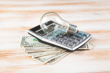 calculator, money and light bulb on wooden background