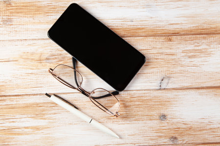 on a wooden background phone, glasses and penの写真素材