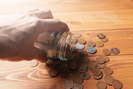 Coins are spilled from a glass bottle on a wooden table