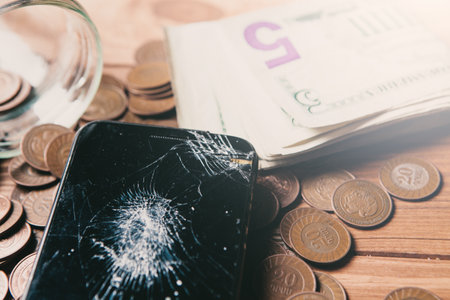 coins from a bottle and a broken phone on the table. concept waste of savingsの写真素材