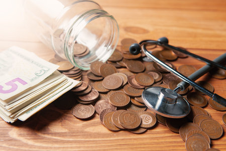 stethoscope on coins and bills pouring from a glass bottle on a tableの写真素材