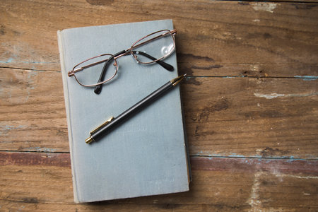 glasses and a pen on a book on a wooden table