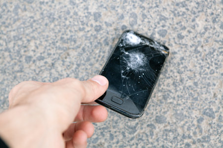 a man picks up a broken phone from the groundの写真素材