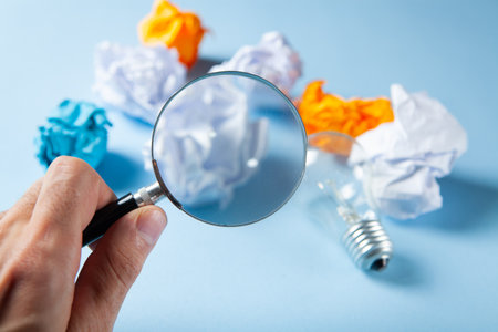 magnifier looks at a lamp and a wad of papers on a blue backgroundの写真素材