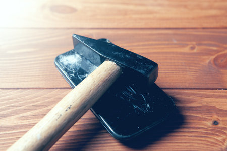 broken smartphone screen and hammer on wooden background