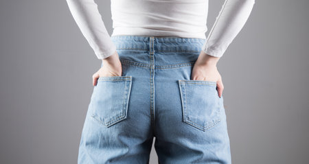 the girl put her hands on the back pockets on a gray background