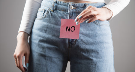 young girl holds the inscription NO between her legs on a gray background