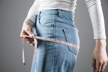 young girl measures waist girth on gray background