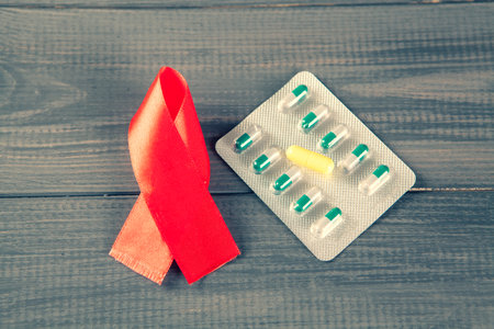 red tape and pills. a symbol of the fight against AIDS, on a gray wooden background