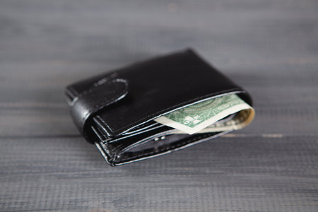 black wallet with money on a gray wooden table