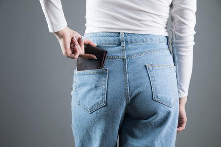 young woman pulls out her wallet from her pocket on a gray background