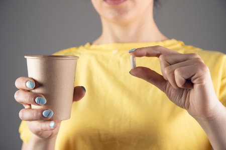 a girl in a yellow dress holds a pill and a glass of waterの写真素材