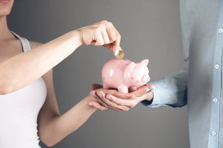 couple holds a piggy bank in their hands on a gray backgroundの写真素材