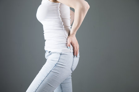 young woman posing with her hands on her back on gray background