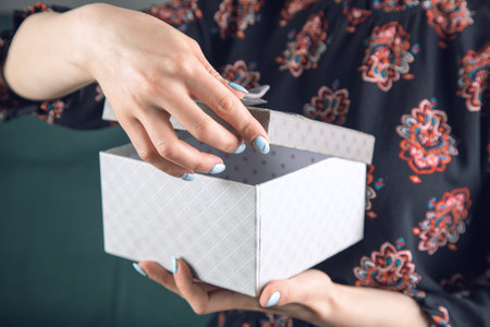 young girl in a dress opens a gift box sitting on the couch
