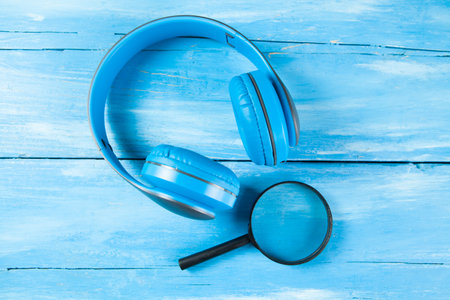 headphones and loupes. audio file search concept on blue wooden background