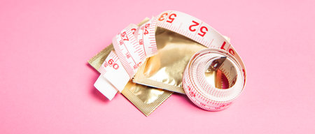 condom and measuring tape on pink background