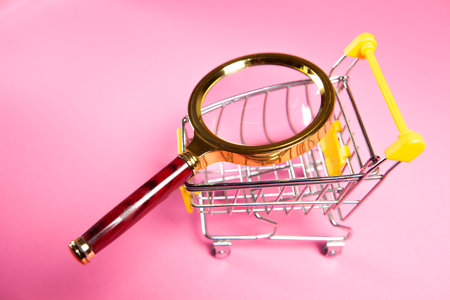 trolley and magnifier on a pink background. shopping search conceptの写真素材
